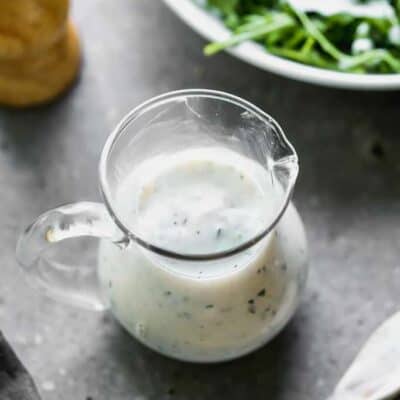 A small dressing pitcher with ranch dressing, next to a salad.