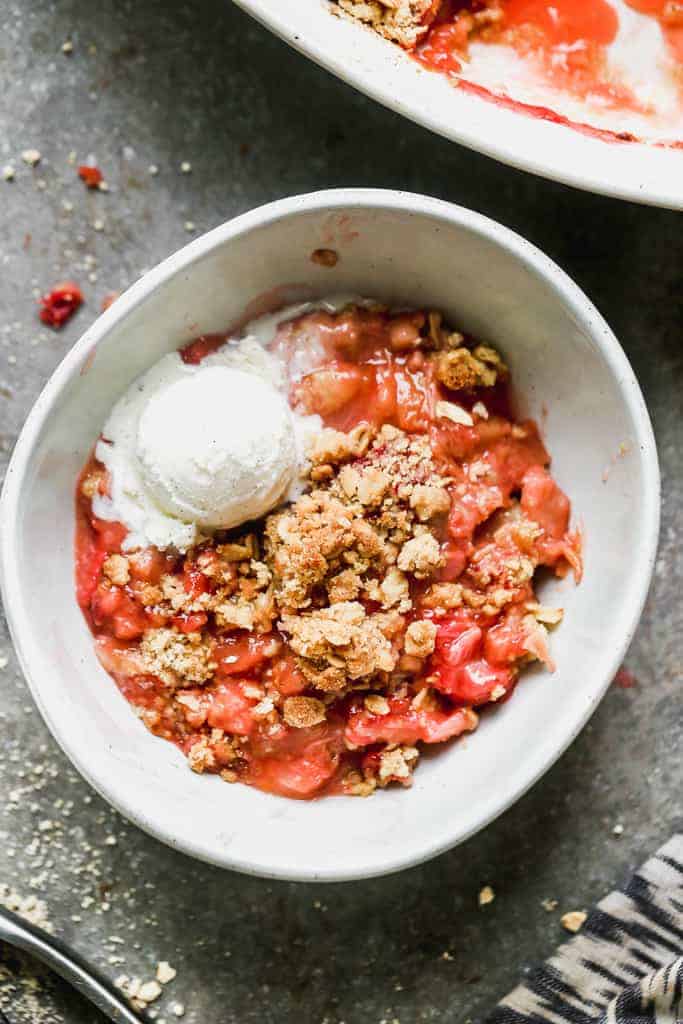 A bowl with warm rhubarb crisp and a scoop of vanilla ice cream in it.
