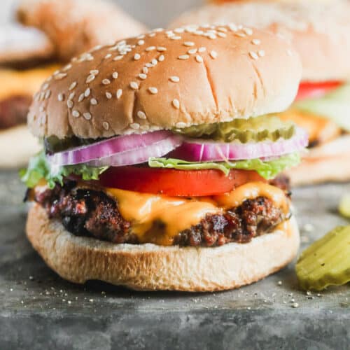 A hamburger in a sesame bun with cheese, tomato, lettuce, onion and pickle.