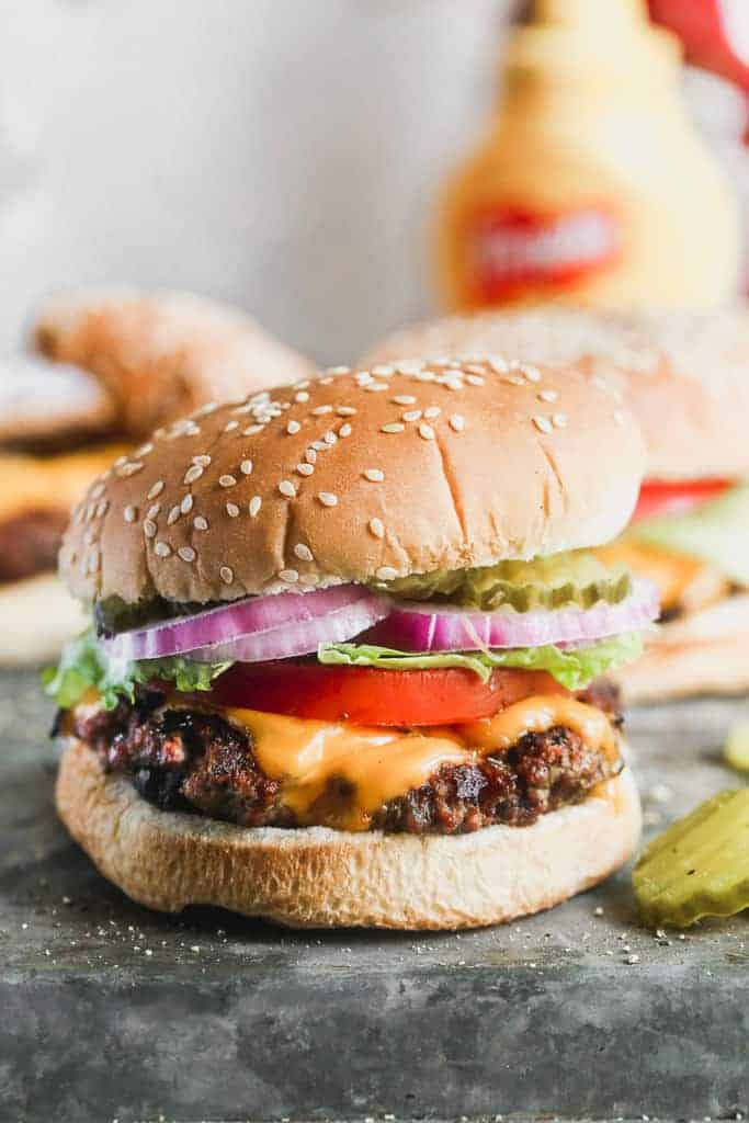 A hamburger in a sesame bun with cheese, tomato, lettuce, onion and pickle.