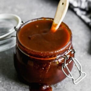 A jar filled with an easy homemade bbq sauce recipe spilling over the edge with a basting brush in it.