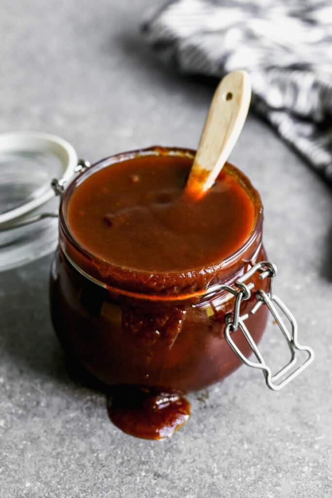 A jar filled with an easy homemade bbq sauce recipe spilling over the edge with a basting brush in it.