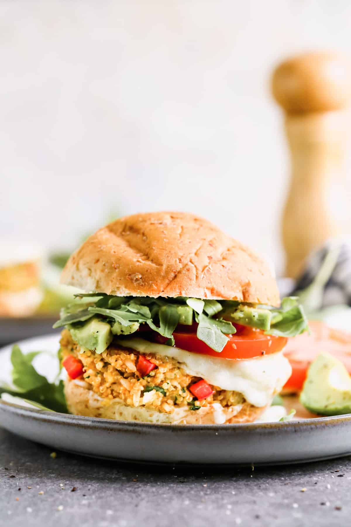 A hamburger Quinoa Burger recipe on a bun with melted provolone cheese, tomato, avocado, and arugula.
