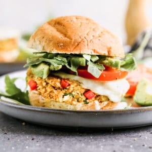 An easy homemade Quinoa Burger recipe served on a bun with melted provolone, arugula, and tomato.