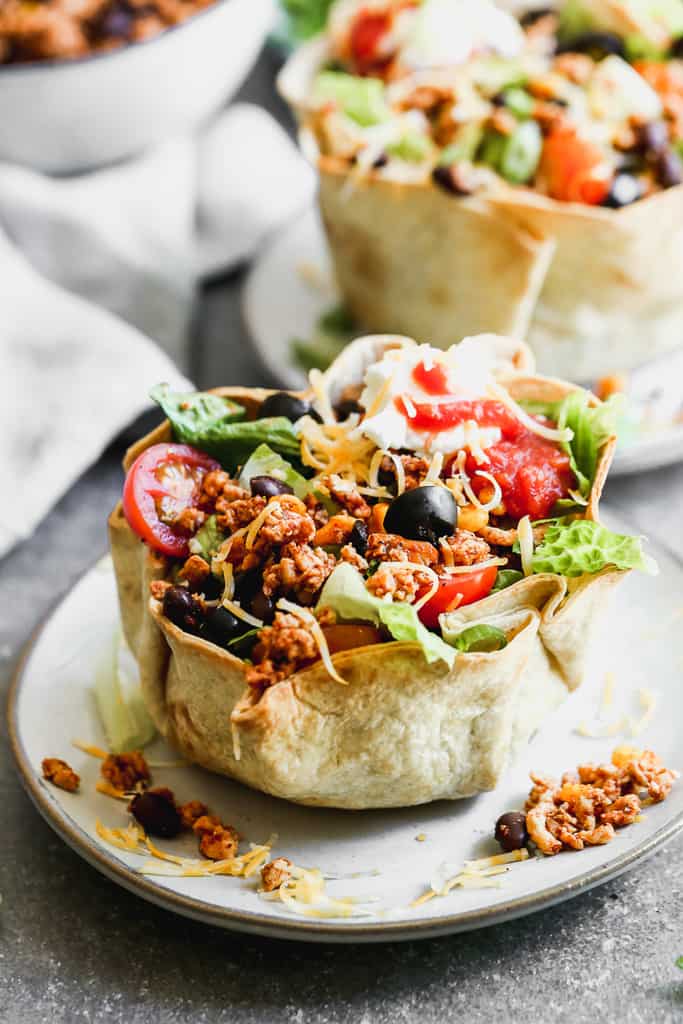 Taco salad served in a baked tortilla bowl, on a plate.