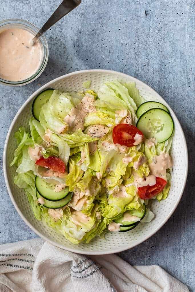 A green salad in a bowl topped with thousand island dressing.