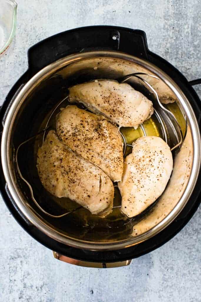 Four cooked chicken breasts resting in the bottom of an instant pot.