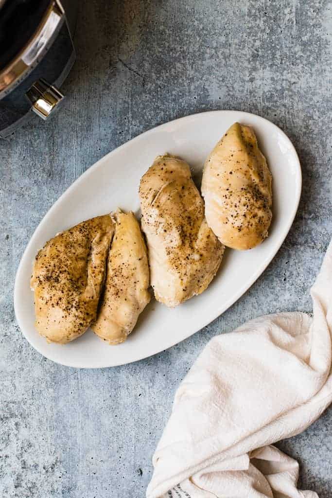 Four cooked chicken breasts on a plate with an instant pot in the background.