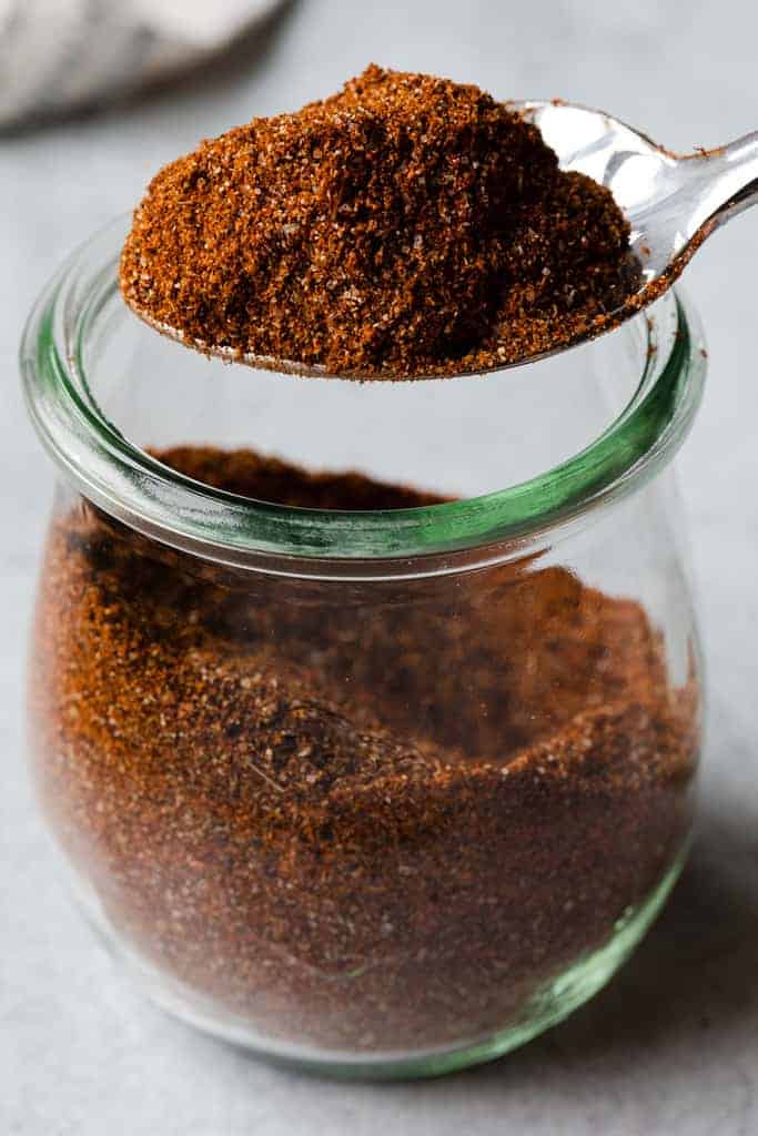 A spice container with homemade taco seasoning lifted out by a spoon.
