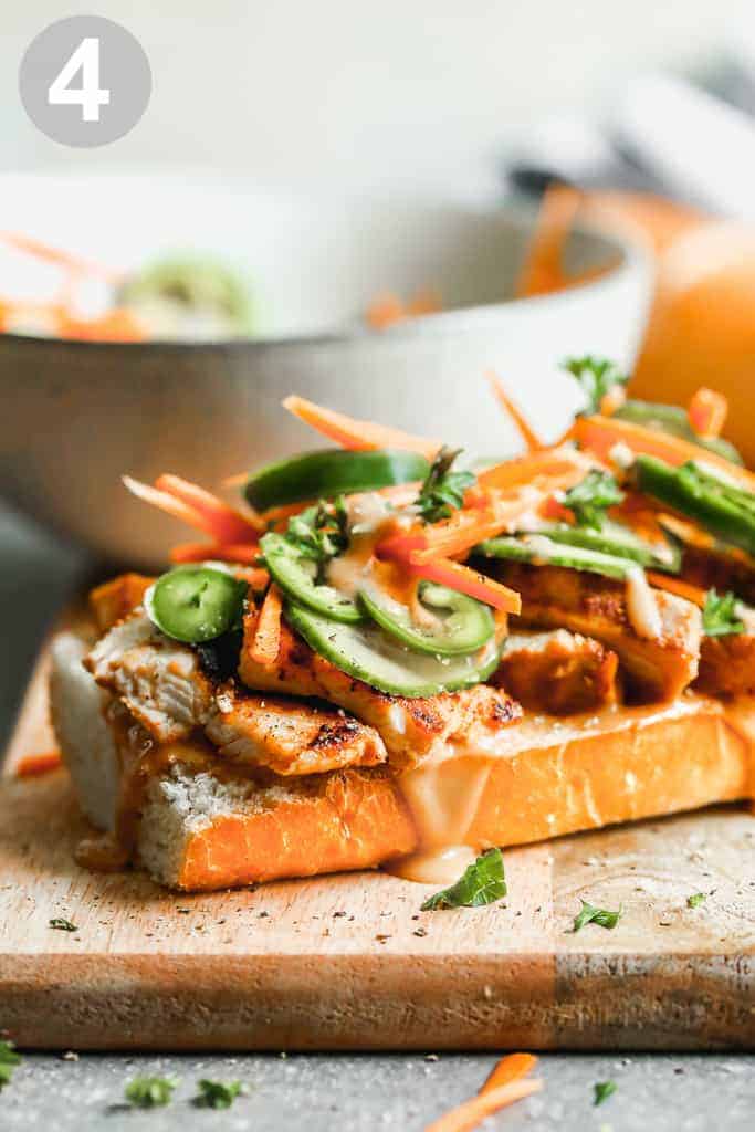 Banh mi sandwich being assembled on a roll with chicken, pickled veggies and sauce.