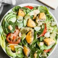Cheeseburger salad in a white bowl, topped with tomato, avocado, onion and dressing.