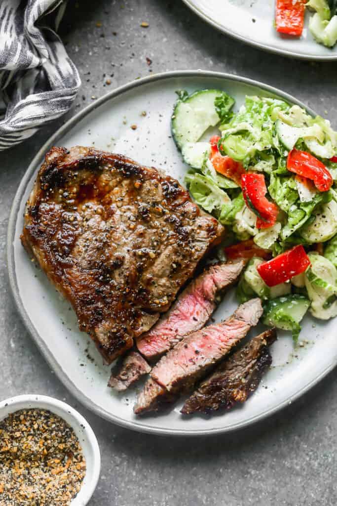 A medium rare grilled steak on a plate with a few slices cut from it and a green salad on the side.