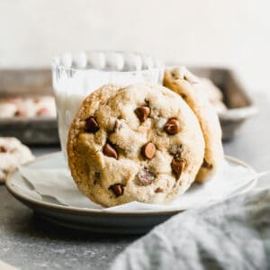 Two of the best Oatmeal Chocolate Chip cookies leaning against a glass of milk on a plate.