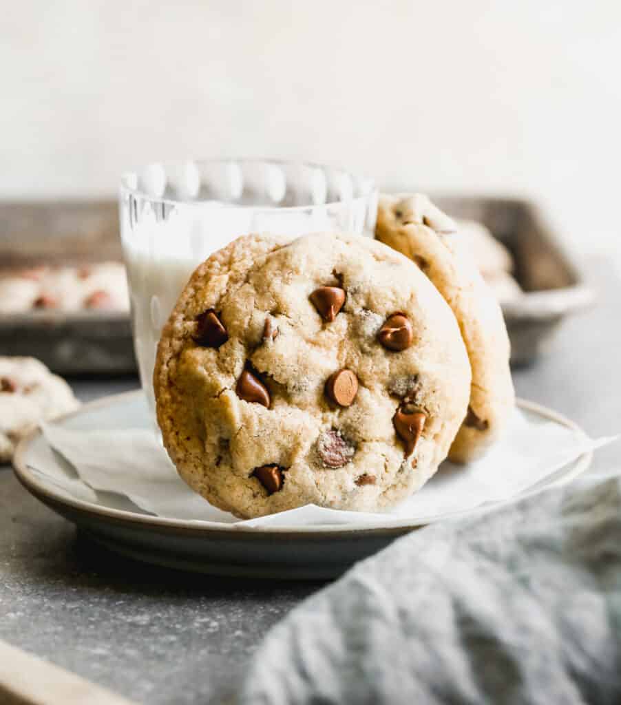 Two of the best Oatmeal Chocolate Chip cookies leaning against a glass of milk on a plate.