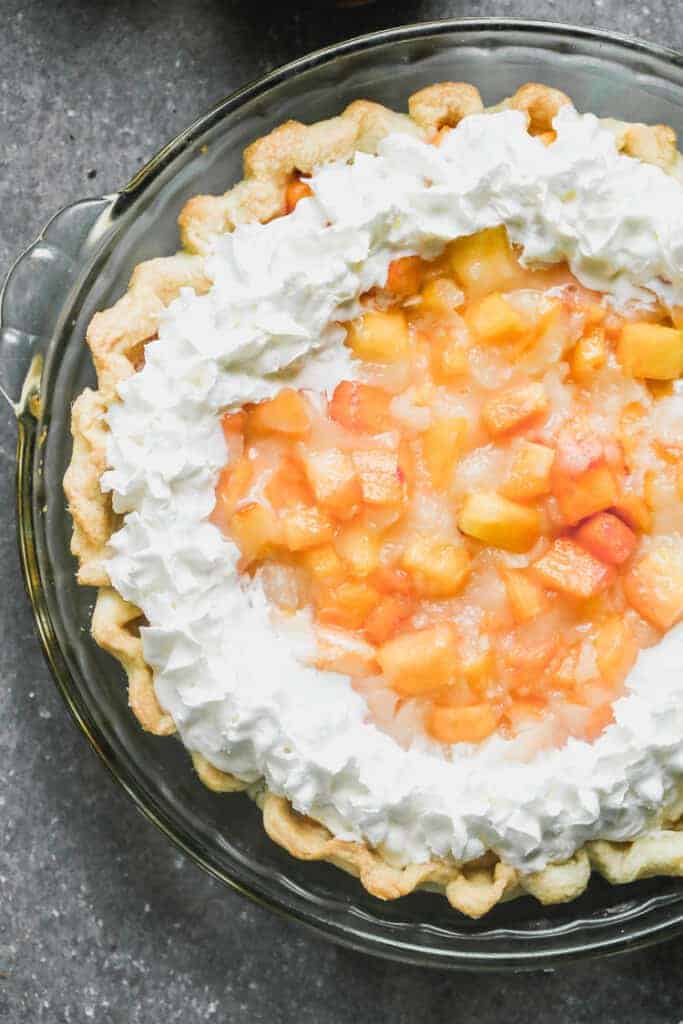 Fresh peach pie in a baked pie shell with whipped cream piped along the edges.