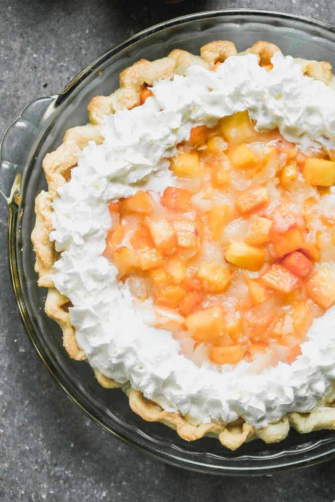 Fresh peach pie in a baked pie shell with whipped cream piped along the top outer rim.