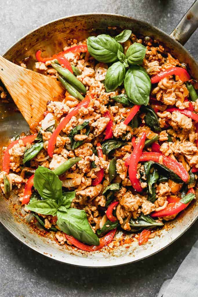 A wok with Thai basil chicken in it, and a wooden spoon for serving.