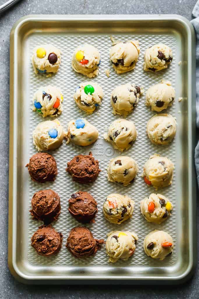 A cookie sheet with four flavors of edible cookie dough on it (M&M, chocolate chip, double chocolate and peanut butter).