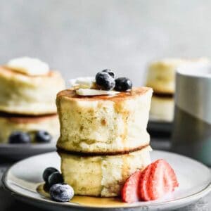 Two Japanese souffle pancakes stacked on each other, on a plate with fresh berries.