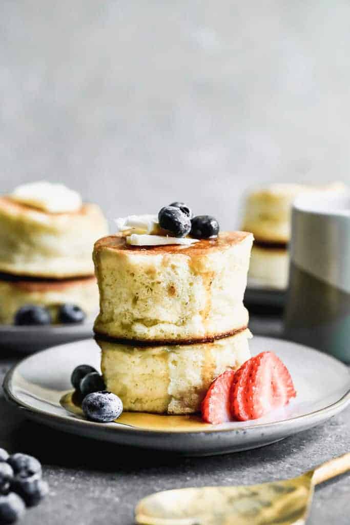 Two Japanese souffle pancakes stacked on each other, on a plate with fresh berries.