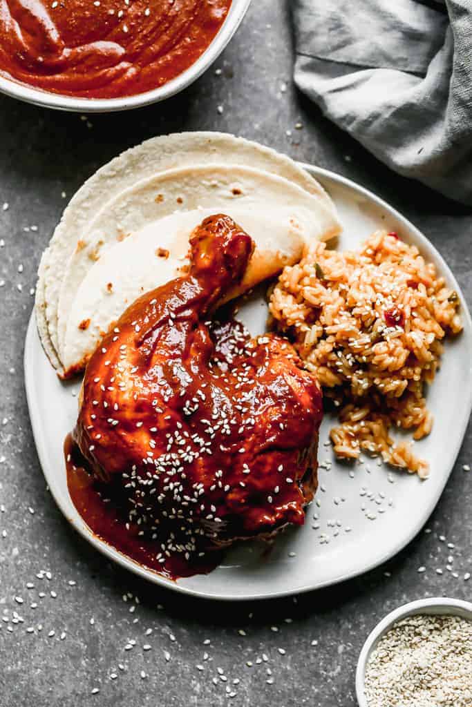 A plate with mole sauce served over chicken with a side of Mexican rice and a tortilla.