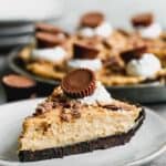 A slice of peanut butter pie on a plate, topped with whipped cream and a Reese's peanut butter cup.