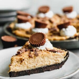 A slice of peanut butter pie on a plate, topped with whipped cream and a Reese's peanut butter cup.