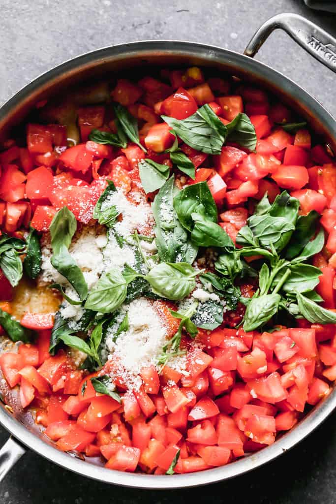 A large skillet with sautéed garlic, fresh tomatoes and basil.
