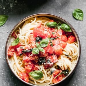 Tomato basil pasta with fresh tomatoes and basil over spaghetti noodles, served in a bowl.