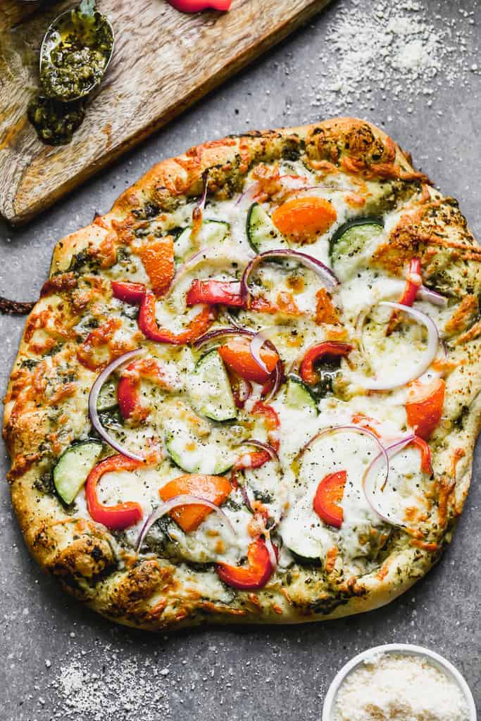 A whole, baked veggie pizza on regular pizza crust with pesto, veggies and cheese.