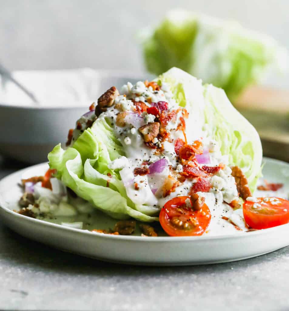 An easy wedge salad on a plate with blue cheese dressing, bacon, onion, and tomatoes.
