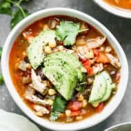 A bowl of fajita soup with chicken, corn and black beans, garnished with fresh avocado and cilantro.