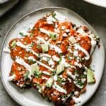 Three mole enchiladas on a plate, garnished with sour cream, cotija cheese, cilantro and avocado.