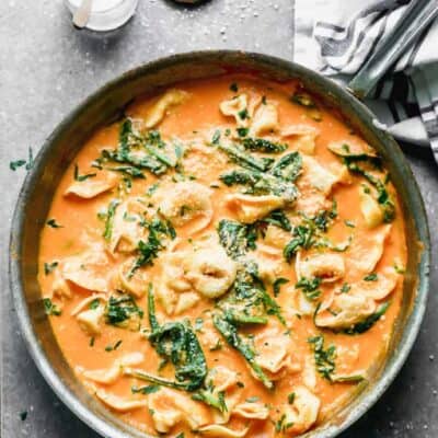 A skillet with roasted red pepper pasta in it including tortellini, spinach and parmesan cheese.