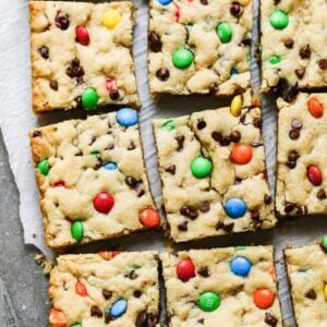 M&M Cookie Bars cut into squares on a board with parchment paper.