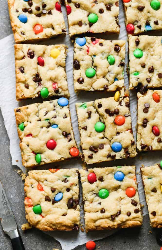 M&M Cookie Bars cut into squares on a board with parchment paper.