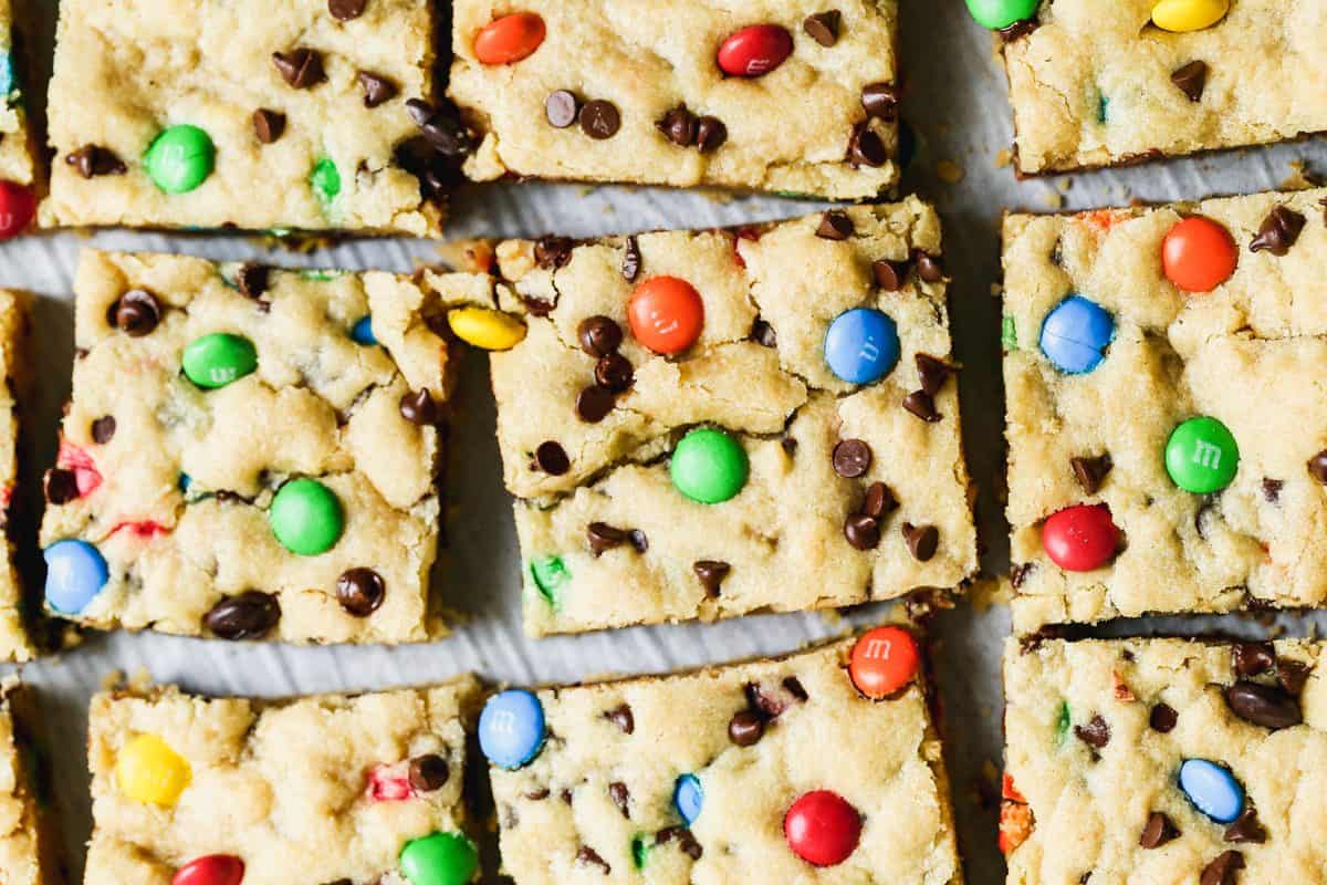 The best M&M Cookie Bars are soft, chewy, and loaded with those colorful candies and mini chocolate chips. Stop scooping cookie dough and bake it in a pan instead!