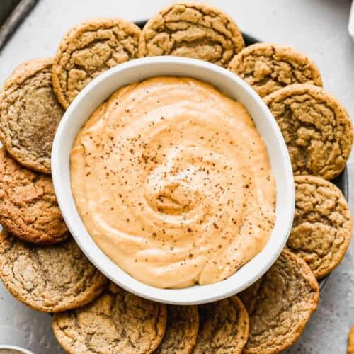 Pumpkin dip in a bowl, on a plate with gingersnap cookies around it.