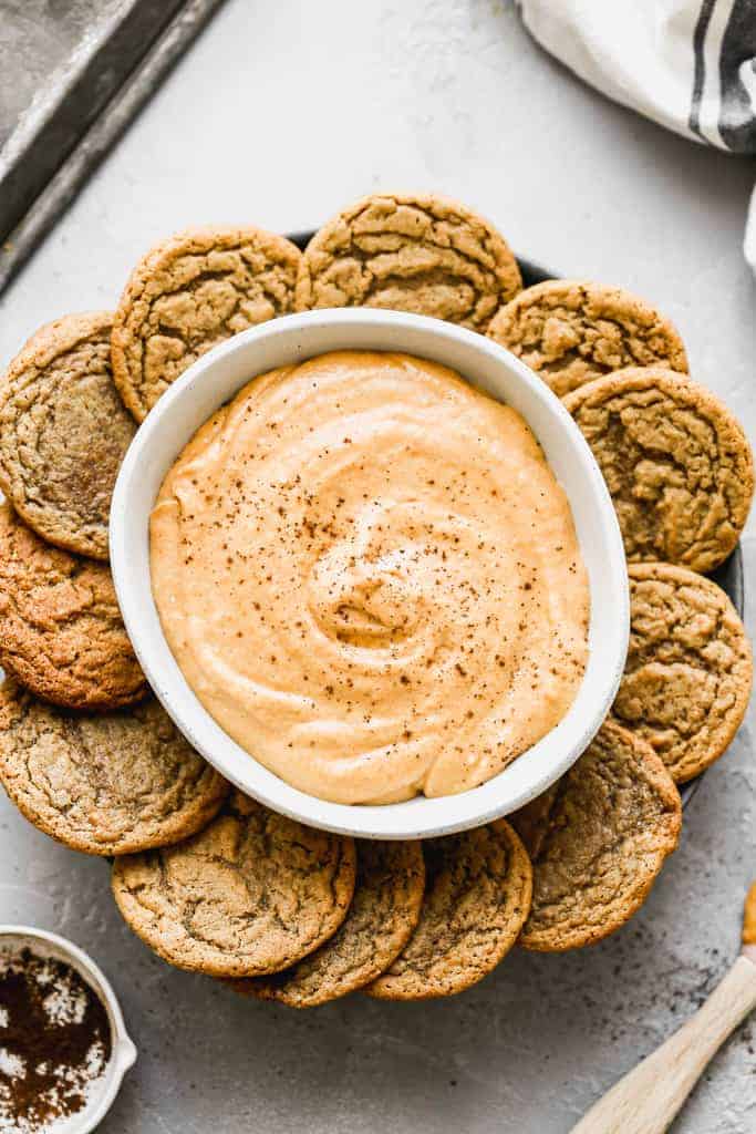 Pumpkin dip in a bowl, on a plate with gingersnap cookies around it.