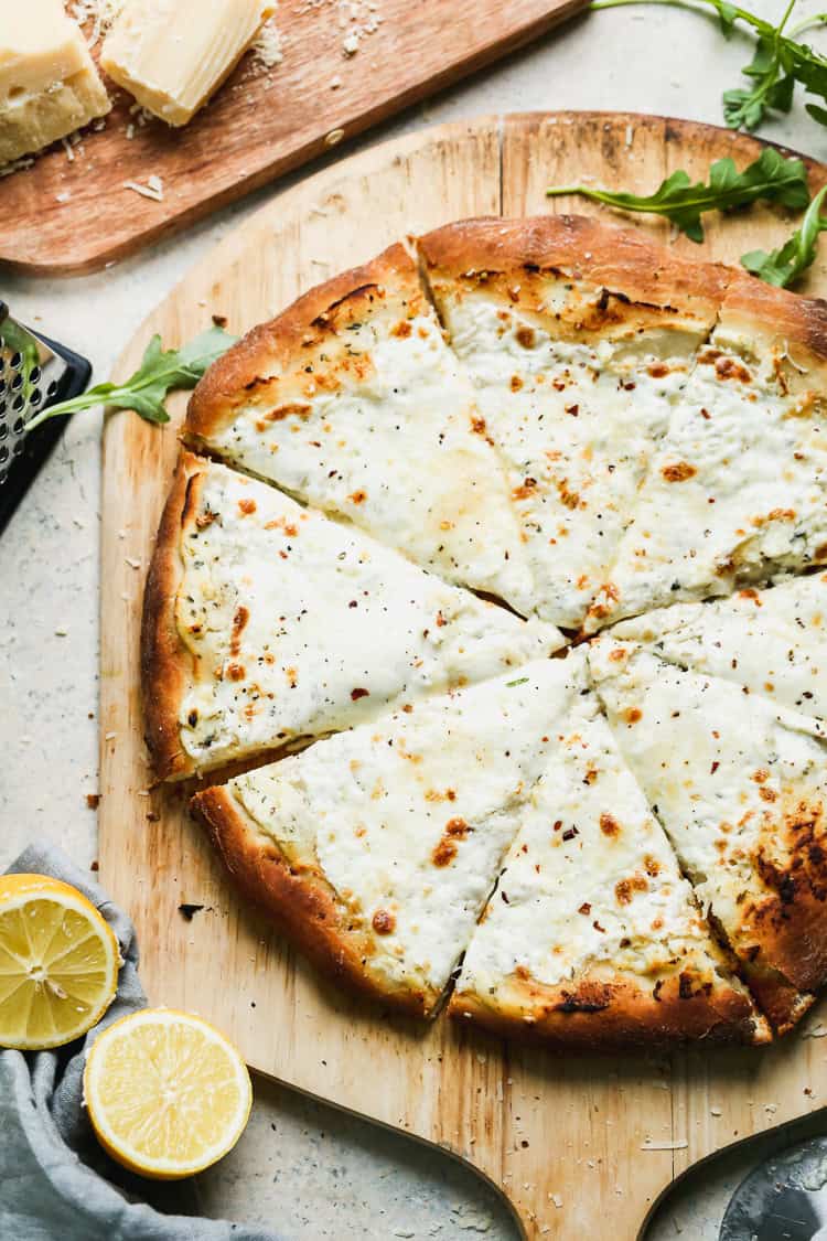 A homemade white pizza made with ricotta cheese and fresh mozzarella, served on a pizza peel. 