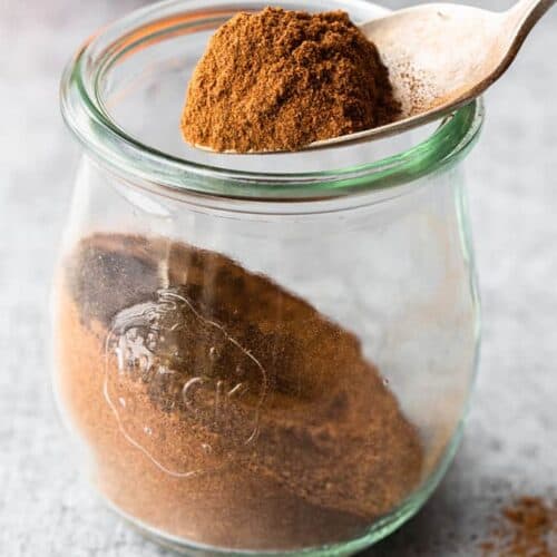 Homemade pumpkin pie spice in a clear glass jar with a spoon lifting some out.