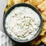 Homemade clam dip in a bowl with potato chips around it.