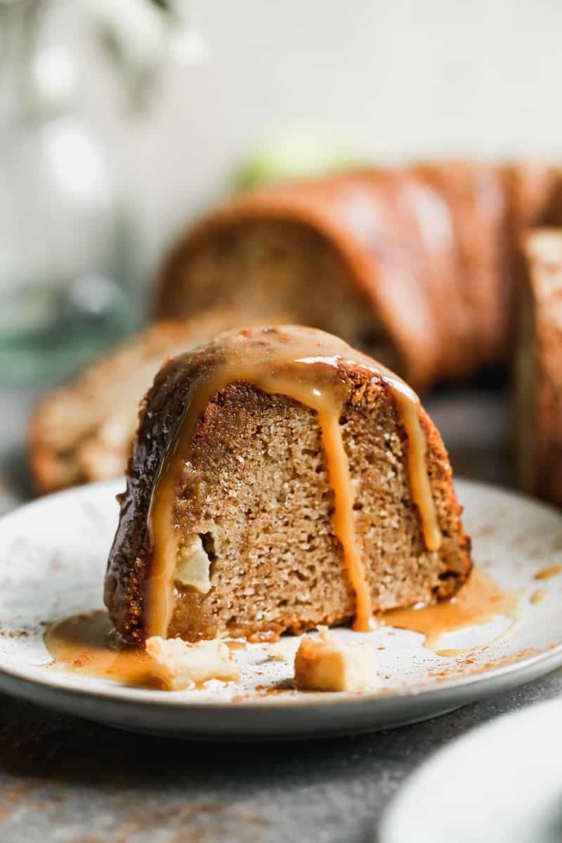 A slice of a fresh Apple Bundt Cake recipe served on a white plate and topped with a homemade caramel sauce.
