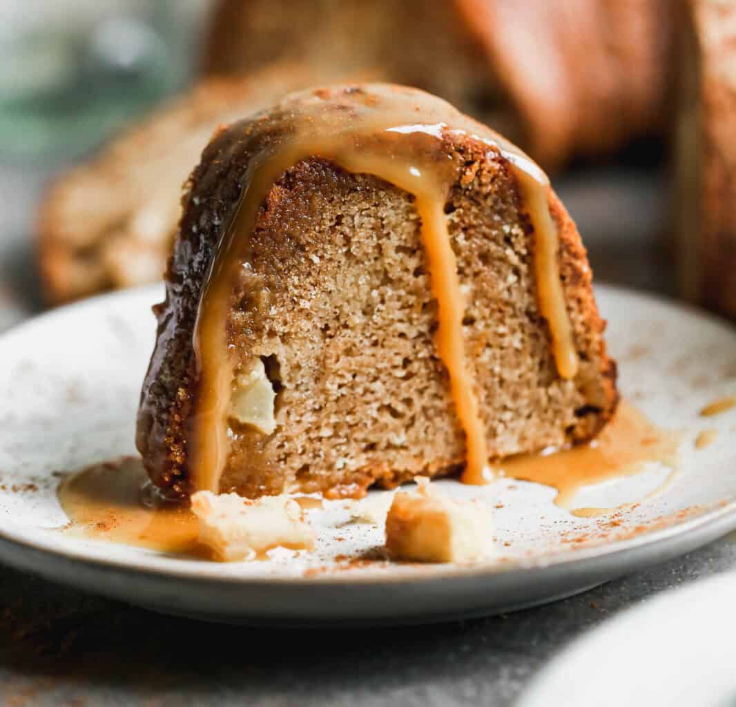 A slice of a fresh Apple Bundt Cake recipe served on a white plate and topped with a homemade caramel sauce.