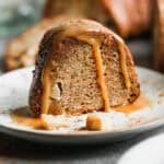 A slice of a fresh Apple Bundt Cake recipe served on a white plate and topped with a homemade caramel sauce.