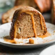 A slice of a fresh Apple Bundt Cake recipe served on a white plate and topped with a homemade caramel sauce.