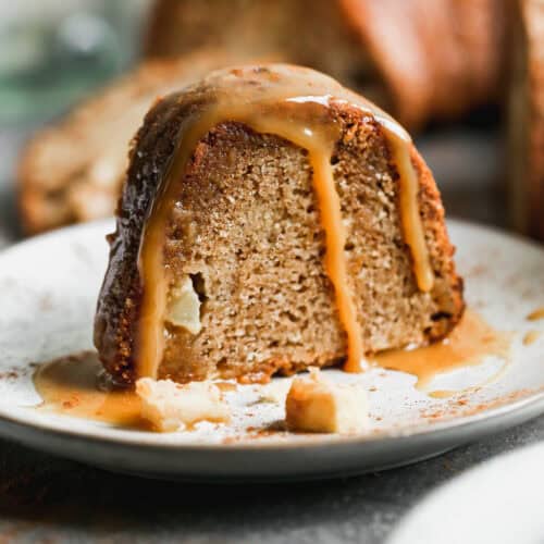 A slice of a fresh Apple Bundt Cake recipe served on a white plate and topped with a homemade caramel sauce.