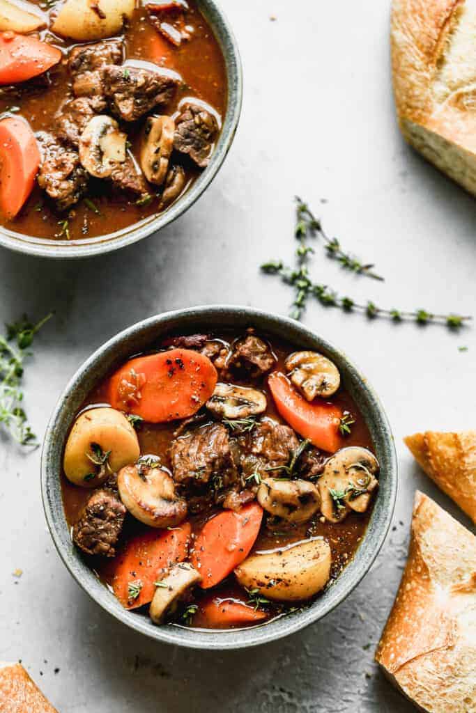Two bowls of beef stew with slices of artisan bread on the side.