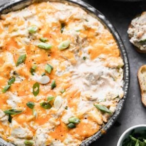 Hot crab dip baked in a round baking dish with cheese on top, and bread slices on the side for dipping.