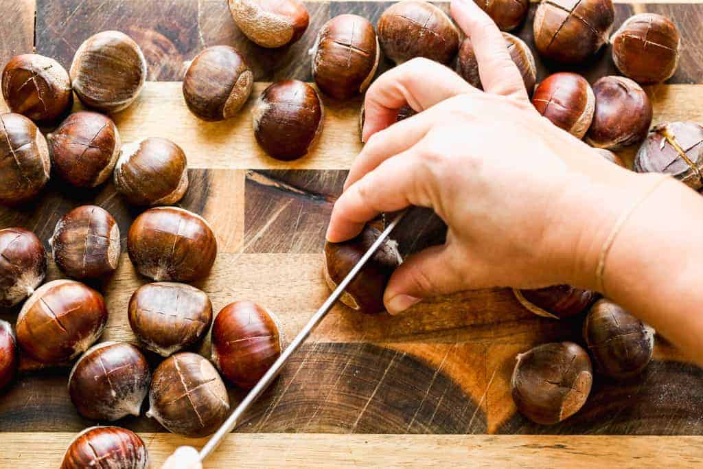 Slits being cut into the top of chestnuts, with a knife.